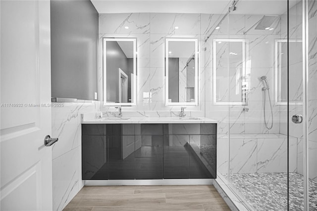 bathroom with a sink, wood finished floors, tile walls, a marble finish shower, and double vanity