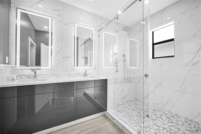 bathroom featuring double vanity, a marble finish shower, wood finished floors, a sink, and tile walls