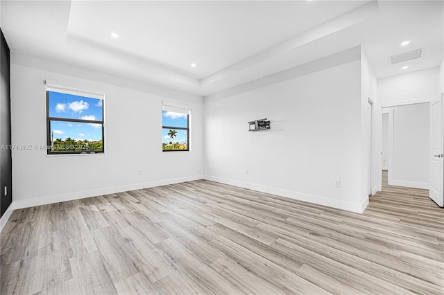 spare room with light wood-style flooring, baseboards, a raised ceiling, and recessed lighting