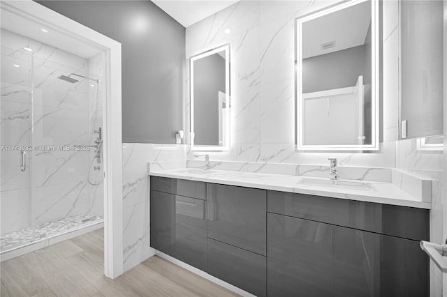 full bath featuring a marble finish shower, double vanity, a sink, and tile walls