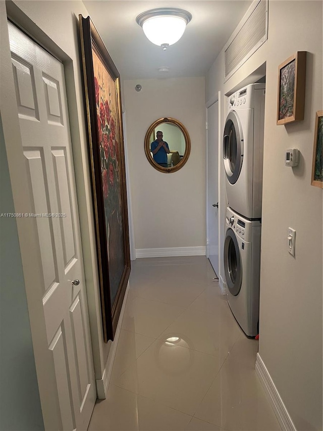 washroom featuring light tile patterned floors, laundry area, stacked washer and clothes dryer, and baseboards