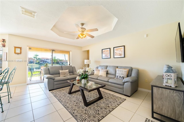 living room featuring a tray ceiling, visible vents, a textured ceiling, and light tile patterned floors