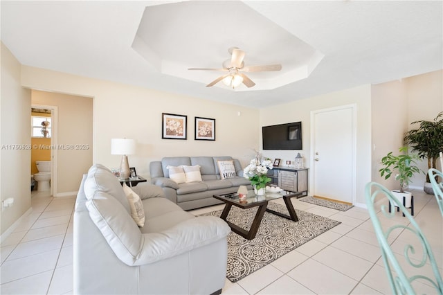 living area featuring light tile patterned floors, a raised ceiling, a ceiling fan, and baseboards