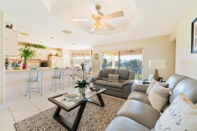 living room with a tray ceiling, a healthy amount of sunlight, visible vents, and light tile patterned floors