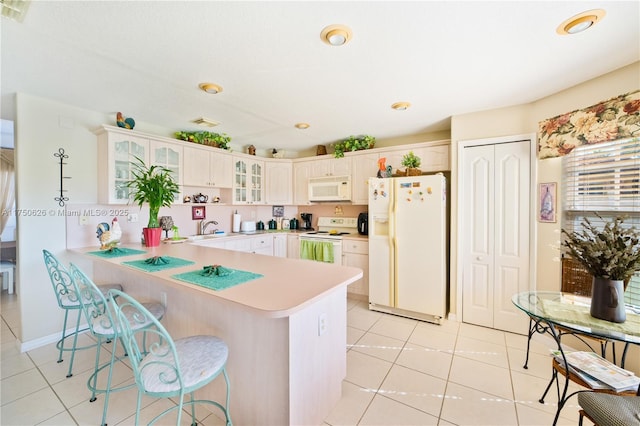 kitchen featuring a peninsula, white appliances, white cabinetry, light countertops, and glass insert cabinets