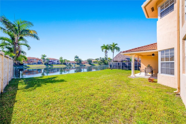 view of yard with a water view, a patio area, a fenced backyard, and a ceiling fan