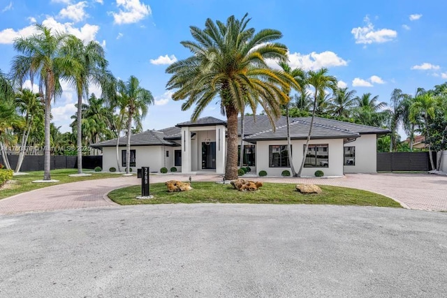 prairie-style home with a front yard, fence, decorative driveway, and stucco siding