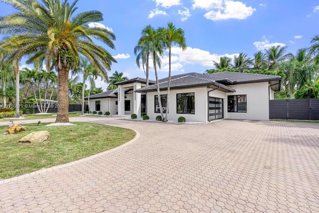 view of front of property featuring a tile roof, curved driveway, an attached garage, fence, and stucco siding