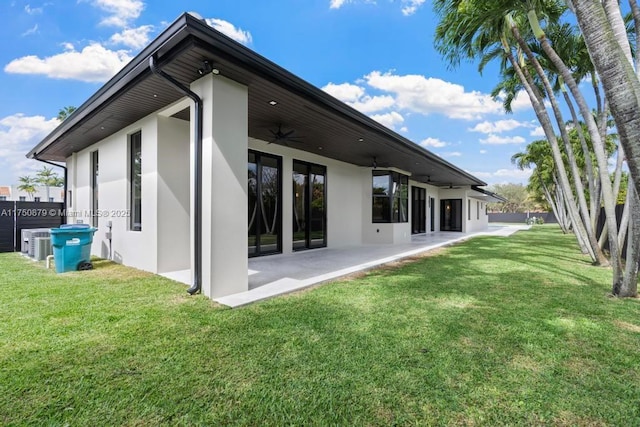 rear view of property featuring ceiling fan, a lawn, a patio, and stucco siding