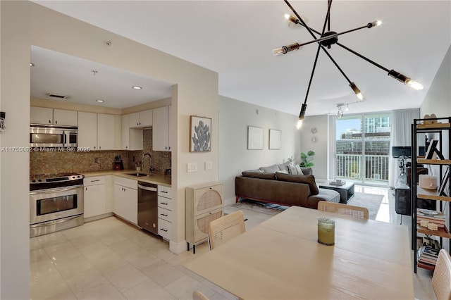 kitchen featuring tasteful backsplash, open floor plan, stainless steel appliances, white cabinetry, and a sink