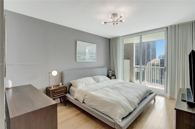 bedroom with access to outside, floor to ceiling windows, light wood finished floors, and an inviting chandelier