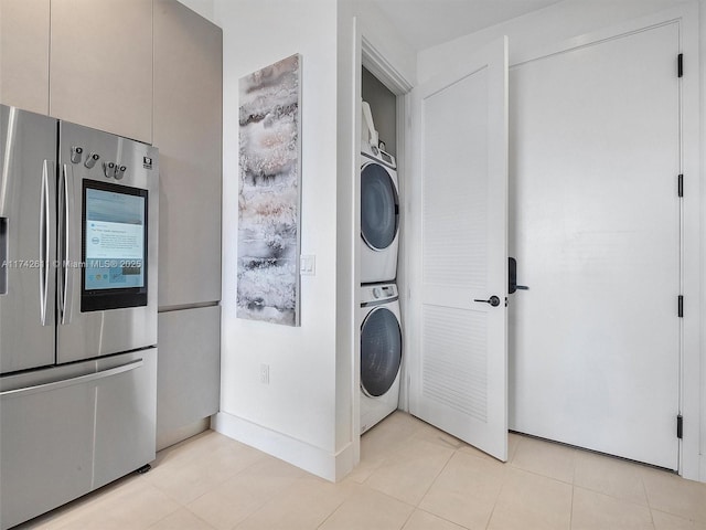 laundry area featuring stacked washer and dryer, baseboards, light tile patterned floors, and laundry area