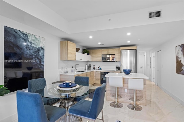 kitchen with appliances with stainless steel finishes, marble finish floor, light countertops, light brown cabinetry, and a sink