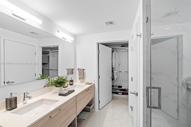 bathroom featuring double vanity, marble finish floor, a walk in closet, and a sink