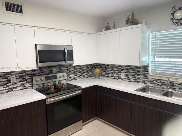 kitchen featuring dark brown cabinetry, visible vents, appliances with stainless steel finishes, light countertops, and a sink