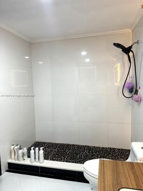 full bath with ornamental molding, tiled shower, tile walls, and toilet