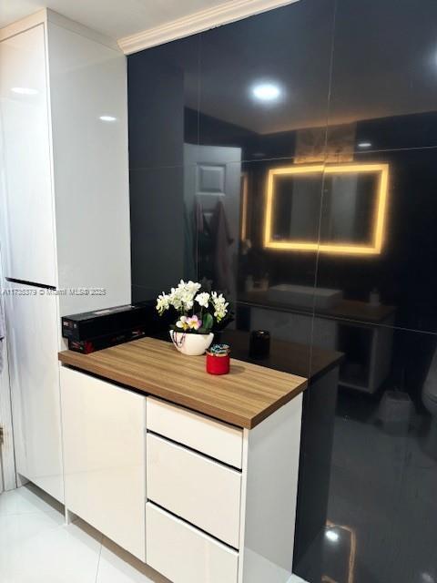 kitchen featuring light tile patterned flooring, butcher block counters, white cabinets, ornamental molding, and modern cabinets