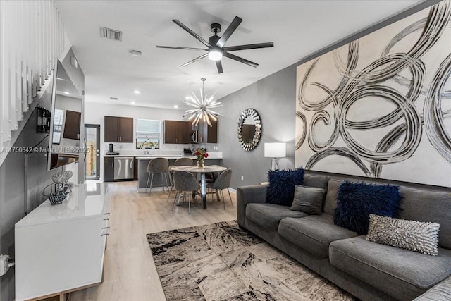 living room featuring recessed lighting, ceiling fan with notable chandelier, visible vents, baseboards, and light wood-style floors