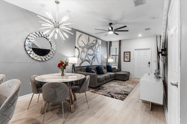 living area featuring ceiling fan with notable chandelier, light wood finished floors, visible vents, and baseboards