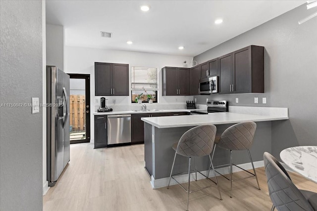 kitchen featuring stainless steel appliances, a breakfast bar, light countertops, and a peninsula