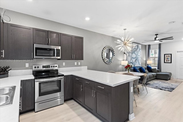 kitchen featuring light wood-style flooring, a peninsula, open floor plan, light countertops, and appliances with stainless steel finishes