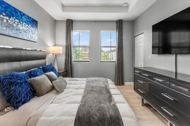 bedroom featuring light wood-type flooring, a raised ceiling, a textured wall, and baseboards