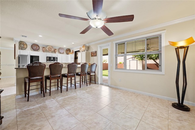 interior space featuring stainless steel microwave, a breakfast bar, ornamental molding, and visible vents