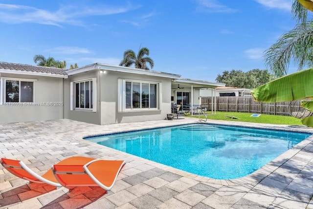 view of swimming pool featuring a lawn, a fenced in pool, ceiling fan, fence, and a patio area