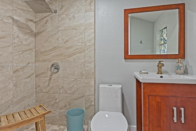 full bathroom featuring a textured wall, a tile shower, vanity, and toilet