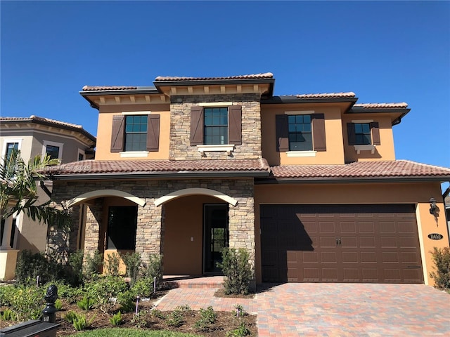 mediterranean / spanish-style house featuring decorative driveway, an attached garage, a tile roof, and stucco siding