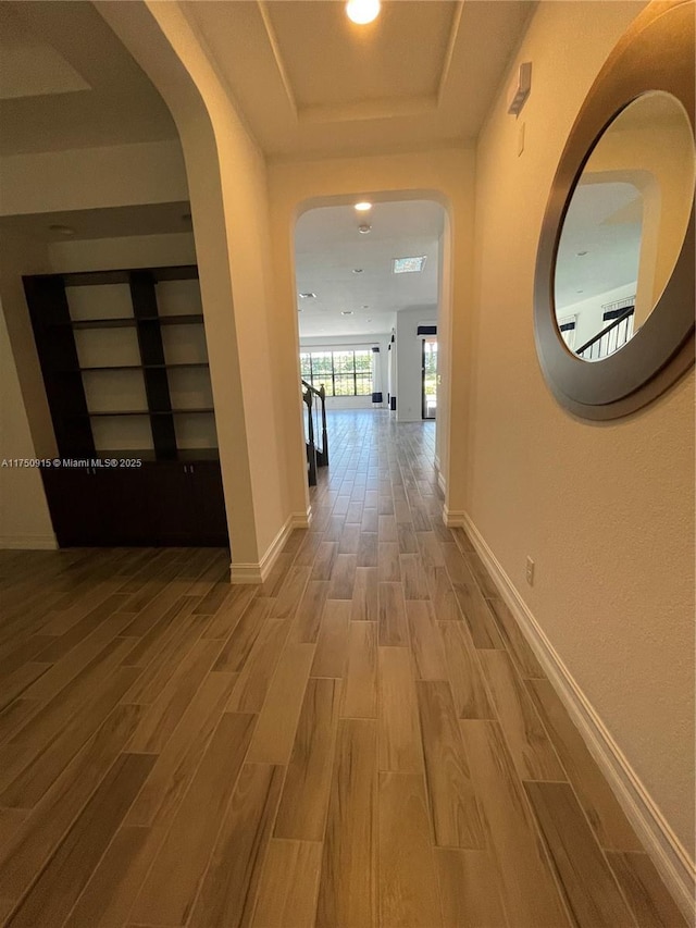 corridor with recessed lighting, a raised ceiling, baseboards, and wood finished floors