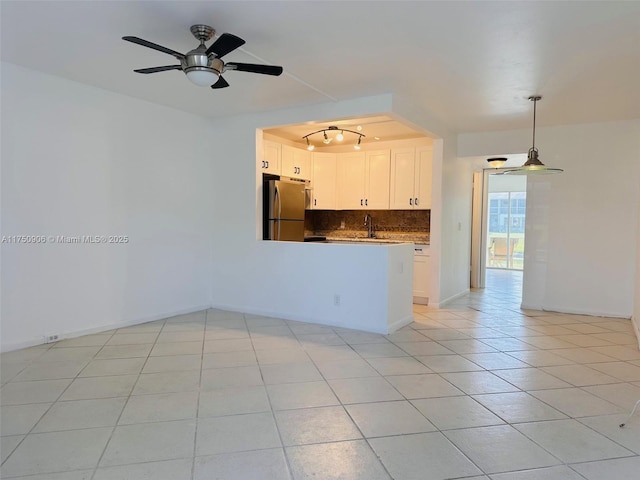 kitchen with light tile patterned floors, freestanding refrigerator, hanging light fixtures, white cabinetry, and backsplash