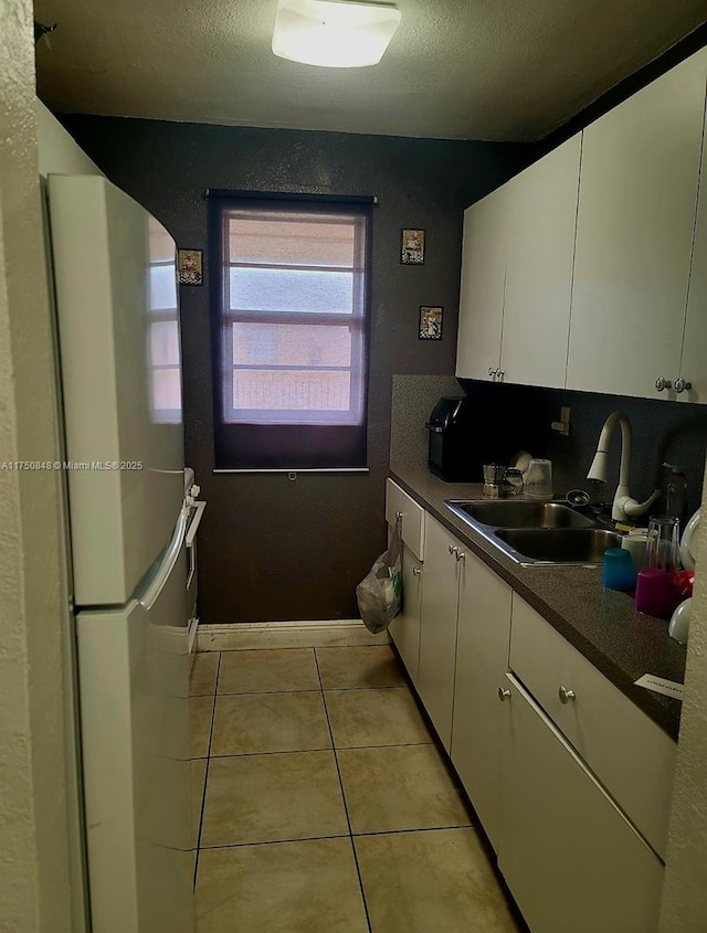 kitchen featuring dark countertops, light tile patterned floors, white cabinetry, and freestanding refrigerator