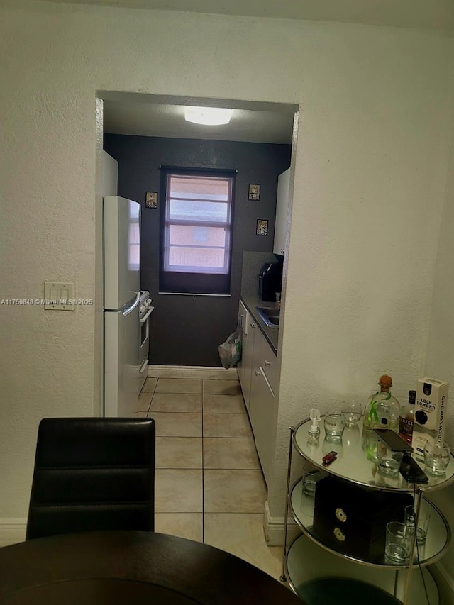 kitchen with light tile patterned floors, light countertops, freestanding refrigerator, a sink, and oven