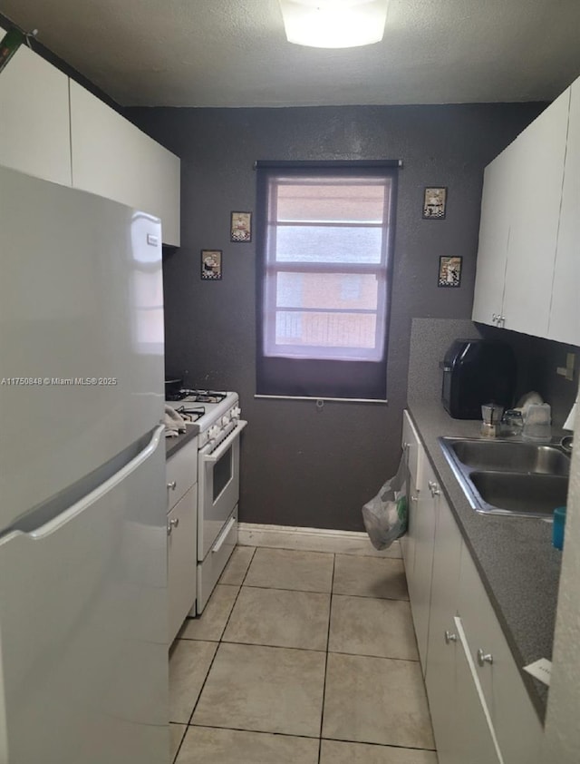 kitchen with light tile patterned floors, white appliances, a sink, and white cabinets