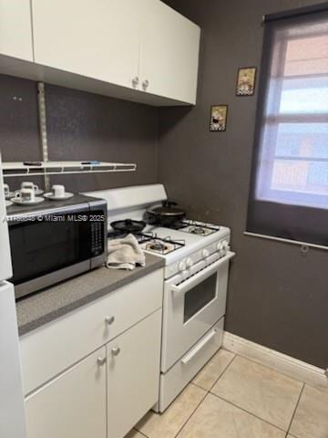 kitchen featuring light tile patterned floors, white range with gas stovetop, white cabinetry, stainless steel microwave, and dark countertops