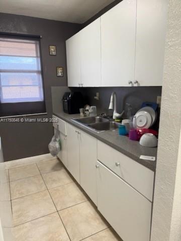 kitchen featuring dark countertops, light tile patterned floors, white cabinets, and a sink