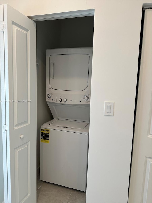 clothes washing area featuring stacked washer / drying machine, laundry area, and light tile patterned flooring