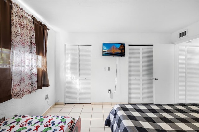 bedroom with light tile patterned floors, visible vents, and multiple closets