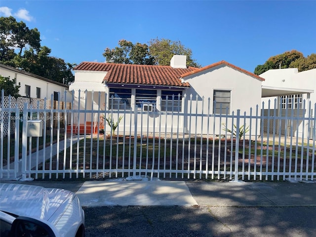 mediterranean / spanish house featuring a fenced front yard, a tile roof, a chimney, and stucco siding