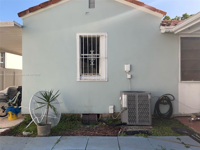 view of side of property featuring a tiled roof, central AC unit, and stucco siding