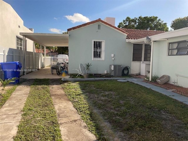 rear view of property featuring a lawn, a tiled roof, fence, central air condition unit, and stucco siding