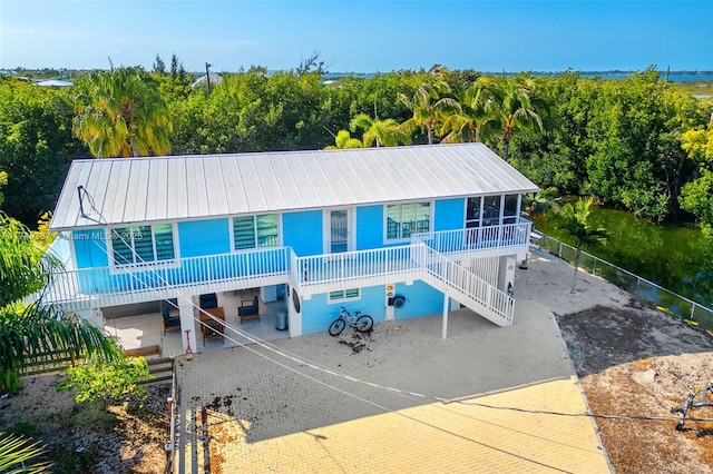 coastal home with stairway, fence, metal roof, and decorative driveway