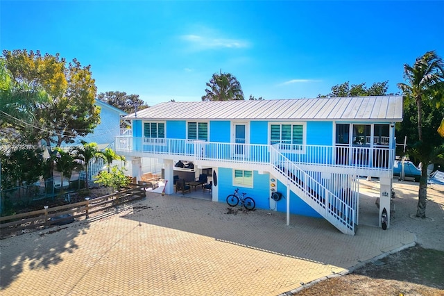 coastal inspired home featuring a patio area, a porch, stairway, and metal roof