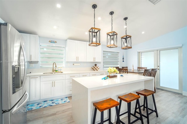 kitchen with a sink, white cabinetry, light countertops, stainless steel fridge with ice dispenser, and pendant lighting