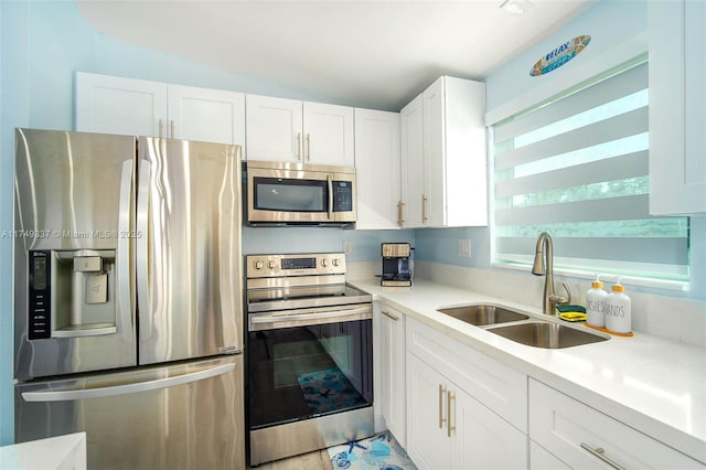 kitchen featuring appliances with stainless steel finishes, white cabinets, light countertops, and a sink