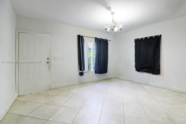 tiled spare room with a chandelier and baseboards