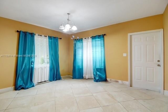 empty room featuring a chandelier, tile patterned flooring, and baseboards