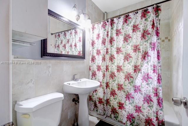 bathroom featuring shower / bathtub combination with curtain, a sink, tile walls, and toilet