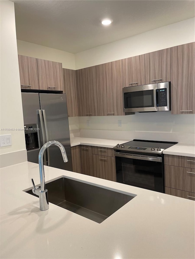 kitchen featuring stainless steel appliances, a sink, light countertops, brown cabinets, and modern cabinets